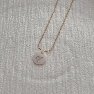 Macro view of a gold snake chain necklace with a shell pendant featuring a cursive Y