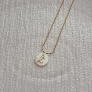 Macro detail of golden snake chain necklace with round white shell and Z letter pendant