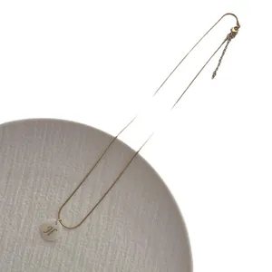 Gold snake chain necklace with natural shell letter H pendant on a white ceramic plate