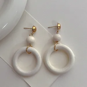Close-up of minimalist white circular wooden hoop earrings with elegant gold metal studs