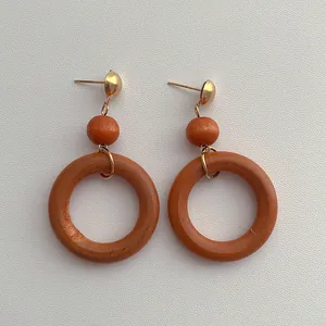 Detail view of retro wooden hoop earrings with golden studs on white textured background