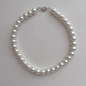 Gros plan d'un collier de perles blanches rondes avec fermoir métallique argenté