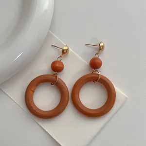 Macro detail of vintage wooden hoop earrings with gold studs and deep orange beads