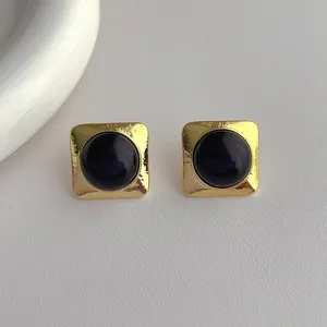 Macro detail of square gold-plated earrings with black gemstone and hammered texture