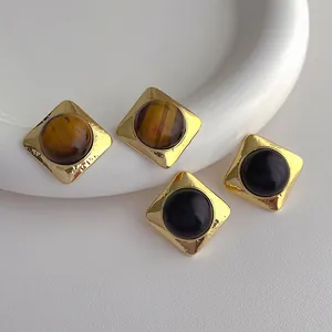 Close-up of vintage square stud earrings with golden textured edges and black gems