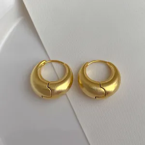 Gros plan de boucles d'oreilles créoles dorées avec texture métal brossé mat