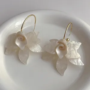 Detail von cremeweißen Acryl-Blumenohrringen mit Goldreifen in einer Schale
