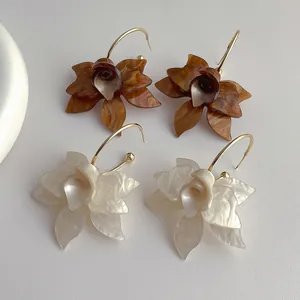 Nahaufnahme eleganter Acryl-Blumenohrringe in Perlweiß und bernsteinfarbenem Braun