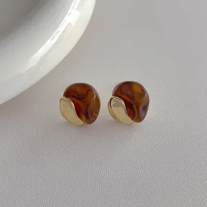 Detailed close-up of resin and gold-tone metal earrings with warm amber textures