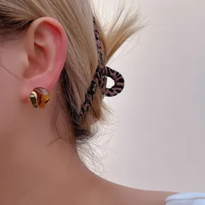 Close-up of elegant gold and amber resin geometric stud earrings worn on the ear