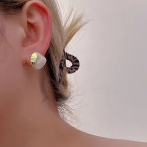 Detail of a minimalist gold metal and white resin geometric earring on a model ear