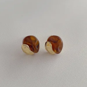 Macro detail of irregular amber resin stud earrings with contrast gold metal texture