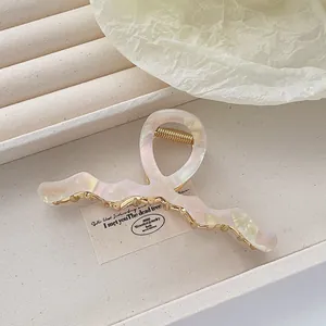 Detail showing wavy pearlescent acetate hair claw clip with golden metal spring base