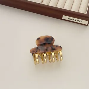 Detail of vintage acetate hair claw with golden metal teeth on a wooden display tray