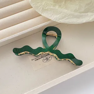 Macro shot of dark green acetate hair claw clip with elegant gold spring and wavy texture