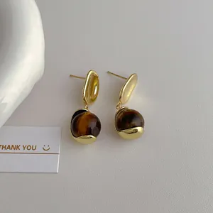 Detail of gold tiger eye drop earrings with S925 silver studs on white background
