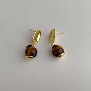 Detailed view of gold earrings featuring tiger eye stone beads and polished metal studs