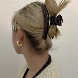 Détail d'une pince à cheveux écaillée avec perles blanches et créoles dorées sur modèle