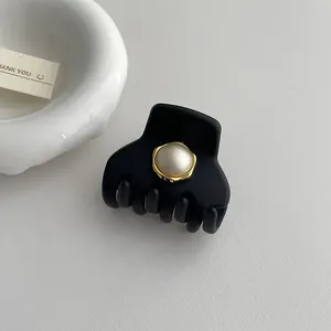 Dettaglio di un fermaglio nero opaco con perla bordata d'oro su sfondo bianco pulito