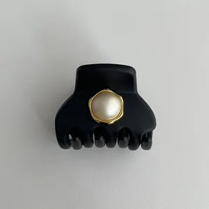 Dettaglio della pinza per capelli nera opaca con perla elegante e cornice in metallo dorato