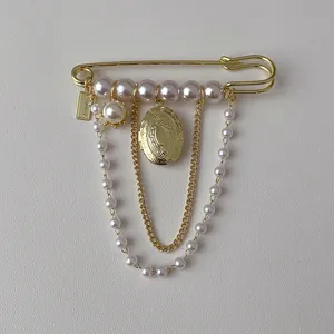Detail of vintage gold safety pin brooch with pearls and hanging locket charm