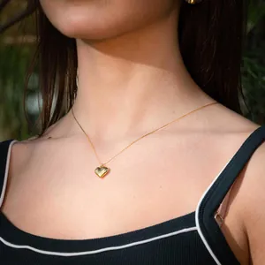 Minimalist gold 3D heart pendant necklace worn by a model in natural sunlight