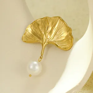 Close-up of golden ginkgo leaf jewelry with brushed texture and a white pearl detail