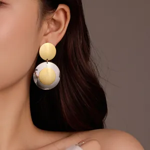 Modern two-tone round metal drop earrings with gold and silver geometric discs on model