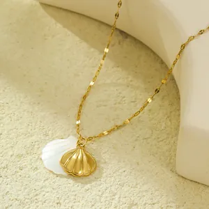 Détail d'un collier pendentif double coquillage doré avec nacre blanche sur un fond de sable