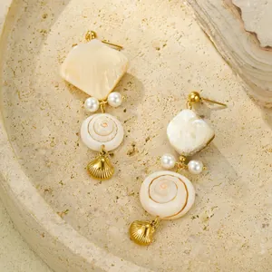 Elegant gold earrings with shell, pearl, and tassel details on a stone tray