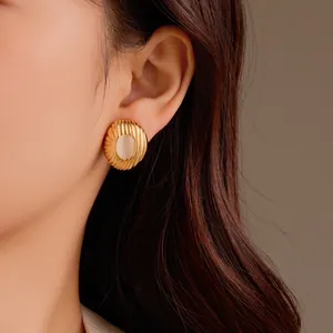 Strukturierte goldene Ohrringe mit weißem Naturstein, getragen von einem Modell