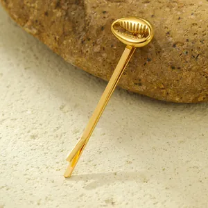 Detailed view of a gold conch seashell hair clip placed on a textured stone surface
