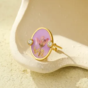 Macro dettagliata dell'anello dorato con ovale in resina viola, fiori secchi e oro