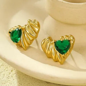 Golden heart earrings with pleated texture and green gemstone center in a close-up shot
