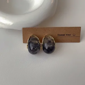 Detail view of water drop resin earrings with gold trim and dark grey ink texture