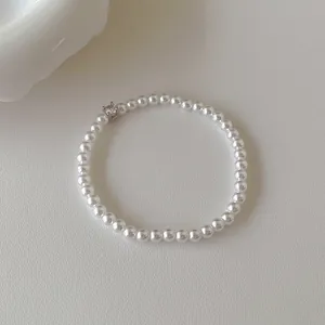 Bracelet élégant en perles blanches avec un zircon central sur un fond beige texturé
