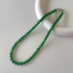 Dettaglio macro di perle di calcedonio verde e chiusura in argento su piatto ceramica