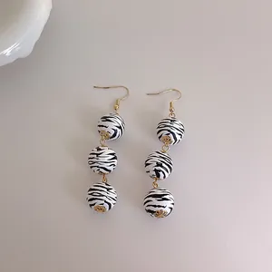 Détail de longues perles en bois zébrées avec des capsules dorées et des crochets d'oreille