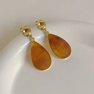 Détail de boucles d'oreilles avec pendentif goutte en résine ambre et métal martelé