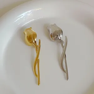 Detailed view of tulip metal brooches in polished gold and silver on a white ceramic plate