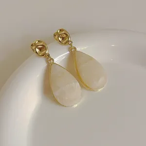 Détail de boucles d'oreilles pendantes avec métal martelé doré et gouttes en acrylique beige
