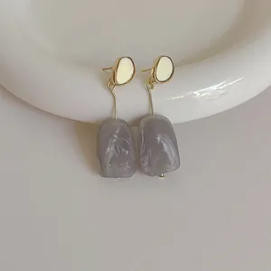 Detail view of long resin drop earrings with gray marble texture and gold metal frame