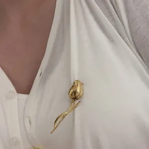 Close-up of golden tulip brooch pinned on white linen fabric showing metallic texture