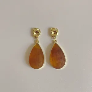 Détail de boucles d'oreilles goutte en acrylique ambré avec texture métal doré martelé
