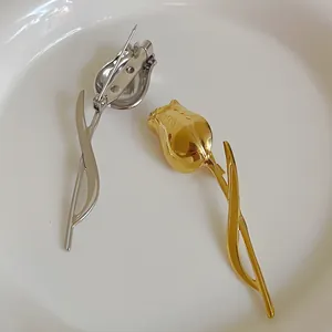 Elegant metal tulip brooches in gold and silver finish on a minimalist white tray