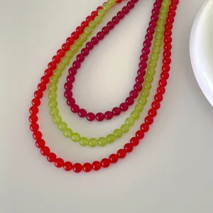 Close-up of vibrant red, light green, and pink agate beaded necklaces in a curved arrangement