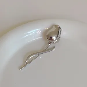 Macro shot of silver tulip flower brooch pin with polished metal texture on white ceramic