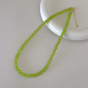 Detail of red agate style beaded necklace with green beads on a ceramic plate