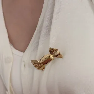 Elegant gold candy-shaped metal brooch pinned on white knitwear for minimalist style