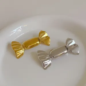 Polished gold and silver candy-shaped metal brooches on a white ceramic plate